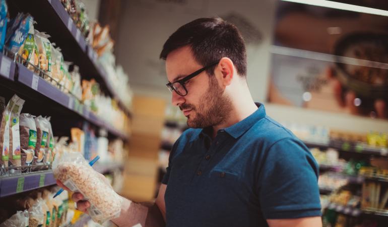 Een consument in de supermarkt leest de ingrediëntenlijst van een voedingsproduct