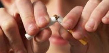 Stoppen met roken wordt verbeeld door twee handen die een sigaret doormidden breken met op de achtergrond vaag een gezicht