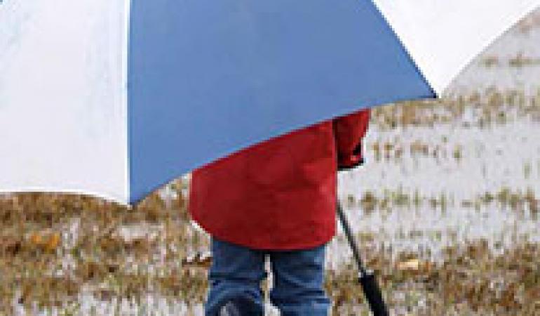 Kind loopt met paraplu door een plas.
