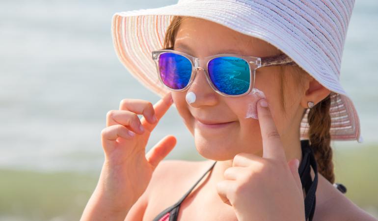 Jong meisje met zonnebrandcreme op gezicht